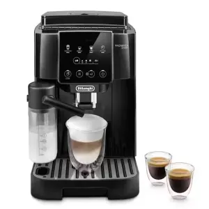 DeLonghi Magnifica Start espresso machine with built-in milk frother pouring a latte into a glass, black finish on a coffee bar setup with two espresso cups nearby.